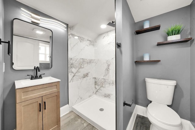 bathroom featuring vanity, wood-type flooring, tiled shower, and toilet