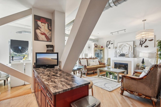 living room featuring an inviting chandelier, track lighting, a tile fireplace, and light wood-type flooring