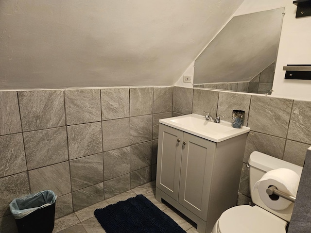 bathroom with vanity, lofted ceiling, tile walls, and toilet