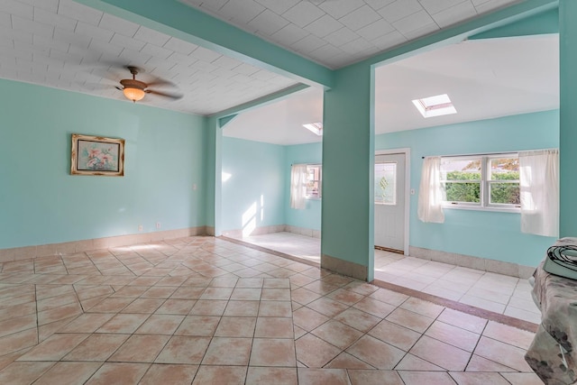 spare room with light tile patterned flooring, ceiling fan, and a skylight