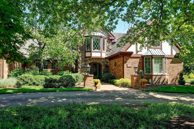 tudor home with stucco siding, a standing seam roof, and brick siding