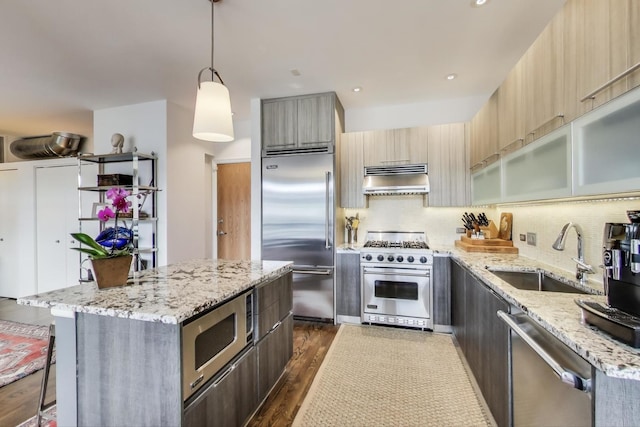 kitchen featuring built in appliances, hanging light fixtures, light stone countertops, under cabinet range hood, and a sink