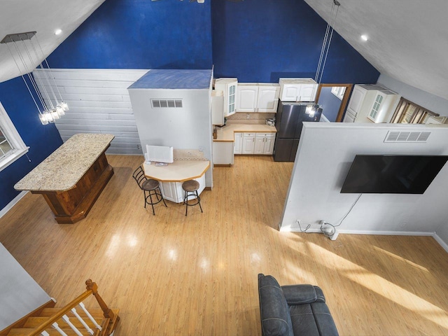 interior space with light wood-style flooring, baseboards, visible vents, and high vaulted ceiling