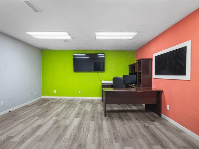 office space featuring an accent wall, wood finished floors, visible vents, and baseboards