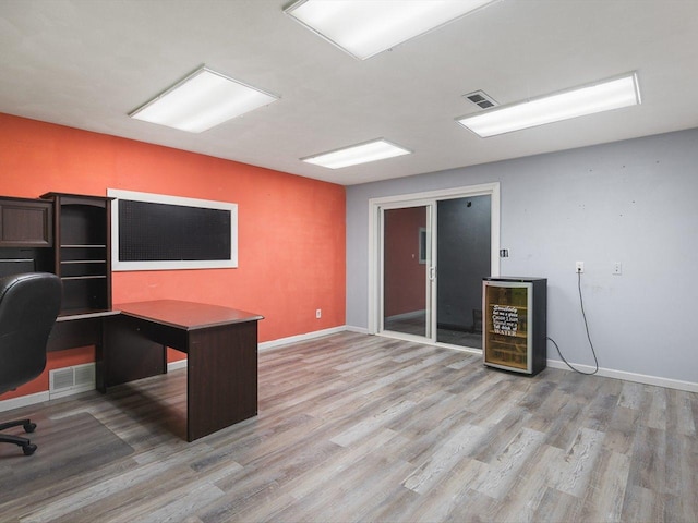 unfurnished office featuring beverage cooler, baseboards, visible vents, and light wood-type flooring