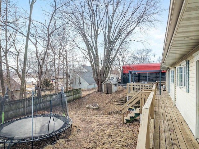 view of yard featuring a wooden deck, a fenced backyard, an outdoor structure, a storage unit, and a trampoline