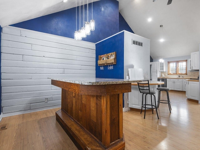 bar featuring visible vents, high vaulted ceiling, hanging light fixtures, and light wood finished floors