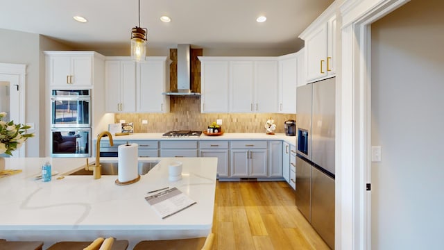 kitchen featuring sink, white cabinets, hanging light fixtures, stainless steel appliances, and wall chimney exhaust hood