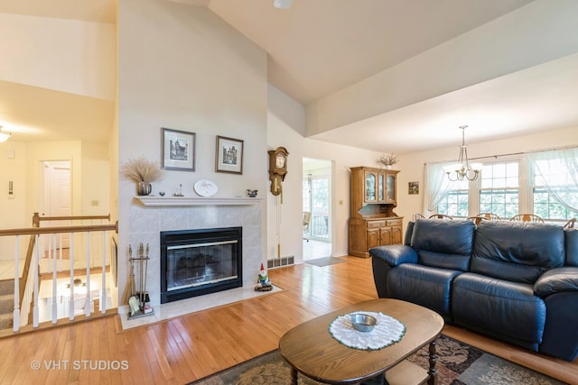 living room featuring an inviting chandelier, hardwood / wood-style floors, a tile fireplace, and high vaulted ceiling