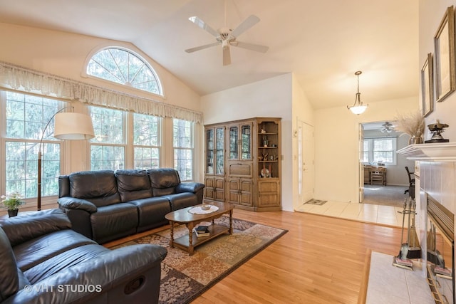 living room featuring a tile fireplace, ceiling fan, high vaulted ceiling, and light hardwood / wood-style flooring