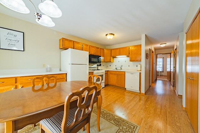 kitchen with white appliances, a sink, light countertops, hanging light fixtures, and brown cabinetry