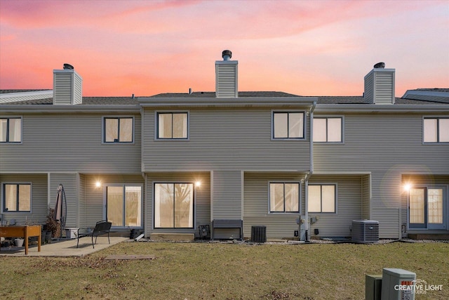 back of house at dusk with a patio area, central AC unit, a chimney, and a yard