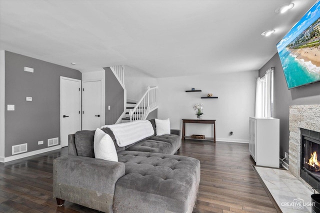 living area featuring visible vents, a stone fireplace, hardwood / wood-style floors, and stairway