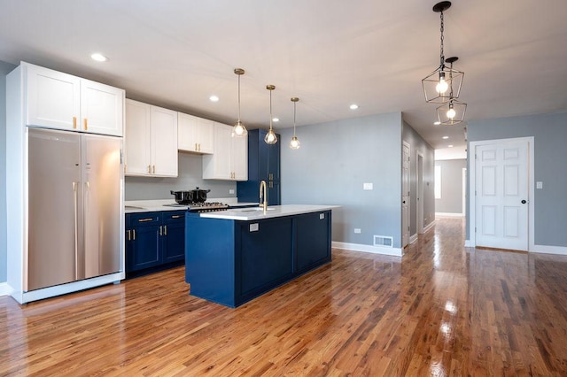 kitchen featuring decorative light fixtures, a center island with sink, paneled built in fridge, and blue cabinets