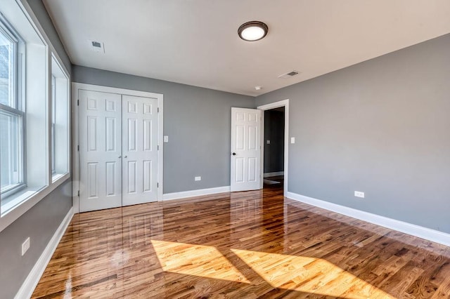 unfurnished bedroom featuring multiple windows, hardwood / wood-style floors, and a closet