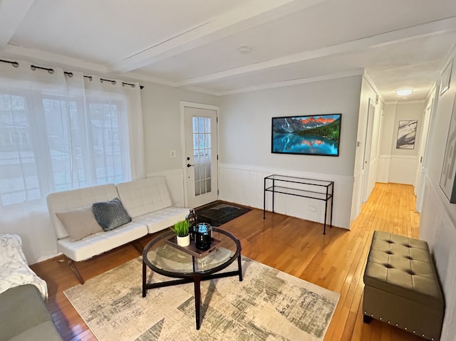 living area with a wainscoted wall, light wood-style flooring, ornamental molding, and beamed ceiling