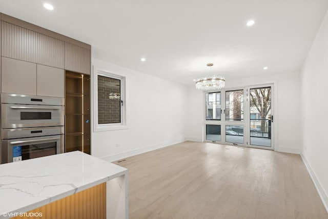 kitchen with double wall oven, light wood-type flooring, light stone counters, and decorative light fixtures