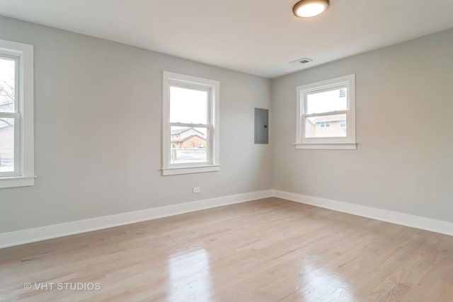 spare room featuring electric panel and light hardwood / wood-style floors