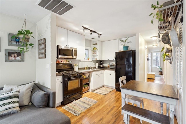 kitchen with sink, black appliances, light wood-type flooring, track lighting, and white cabinets