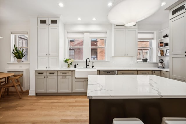 kitchen with white cabinetry, sink, stainless steel dishwasher, light stone counters, and light hardwood / wood-style flooring