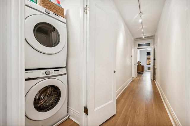 laundry room featuring rail lighting, stacked washer and clothes dryer, and light wood-type flooring