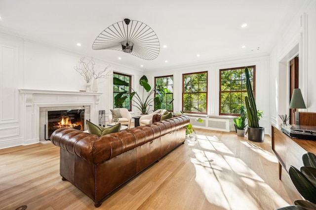 living room featuring ornamental molding, a wealth of natural light, a fireplace, and light hardwood / wood-style flooring