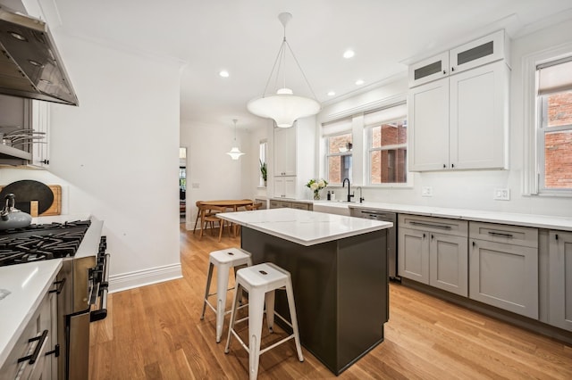 kitchen with a kitchen bar, gray cabinetry, decorative light fixtures, stainless steel dishwasher, and a kitchen island