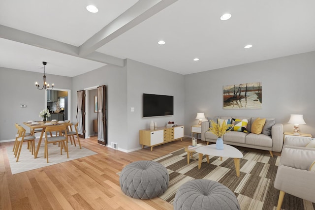 living room with an inviting chandelier, light hardwood / wood-style flooring, and beamed ceiling