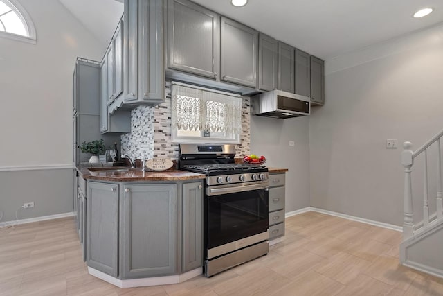 kitchen with tasteful backsplash, stainless steel gas range, ventilation hood, and gray cabinets