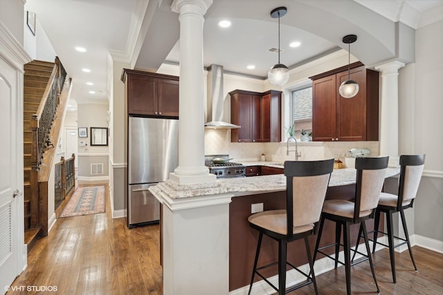 kitchen featuring decorative light fixtures, stainless steel refrigerator, wall chimney range hood, decorative columns, and stove