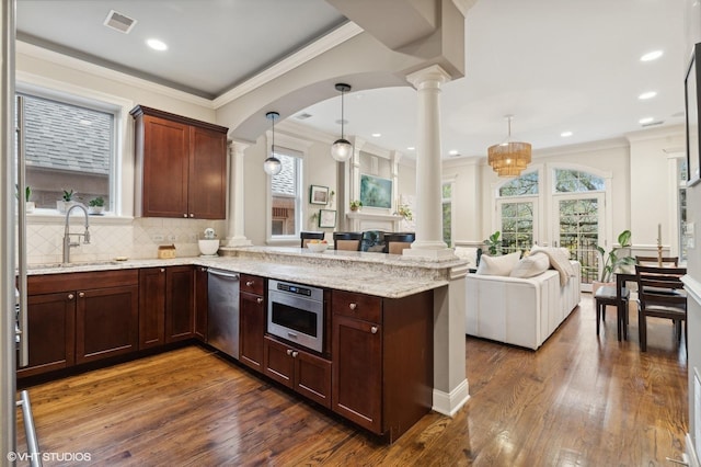 kitchen with decorative light fixtures, kitchen peninsula, sink, and decorative columns