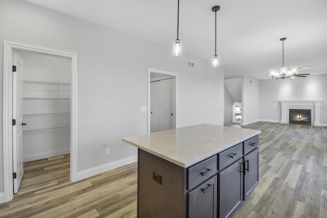 kitchen with a center island, hardwood / wood-style floors, light stone counters, and decorative light fixtures