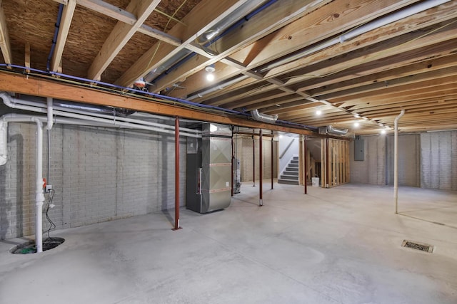 basement featuring heating unit, gas water heater, electric panel, and brick wall