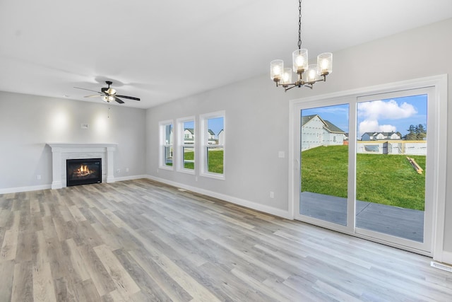 unfurnished living room with ceiling fan with notable chandelier and light hardwood / wood-style floors