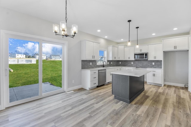 kitchen with white cabinetry, hanging light fixtures, stainless steel appliances, and a kitchen island