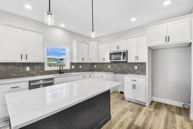 kitchen featuring appliances with stainless steel finishes, pendant lighting, white cabinetry, sink, and light stone counters