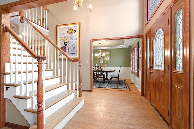 entryway featuring an inviting chandelier, a towering ceiling, and light hardwood / wood-style floors