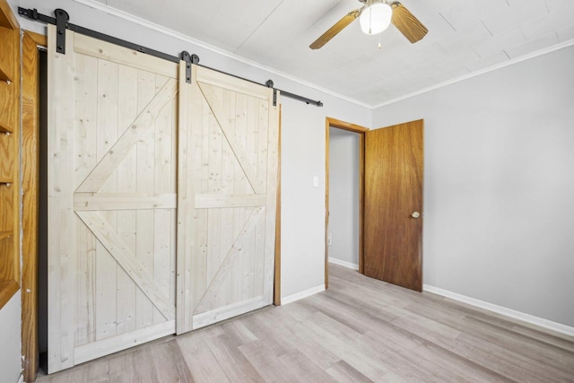 unfurnished bedroom with crown molding, a barn door, ceiling fan, and light hardwood / wood-style flooring
