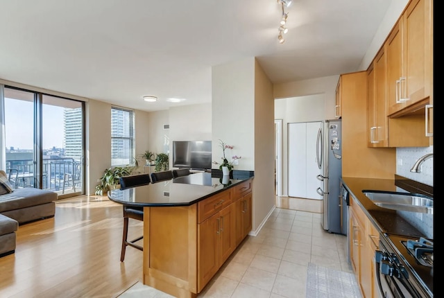 kitchen featuring sink, a breakfast bar area, stainless steel fridge, expansive windows, and stove