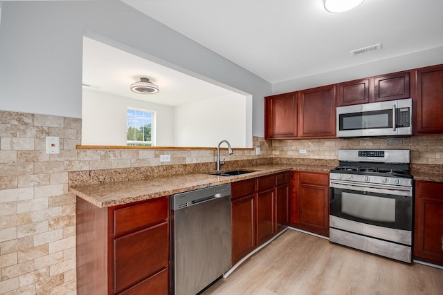 kitchen featuring sink, light stone counters, light wood-type flooring, kitchen peninsula, and stainless steel appliances