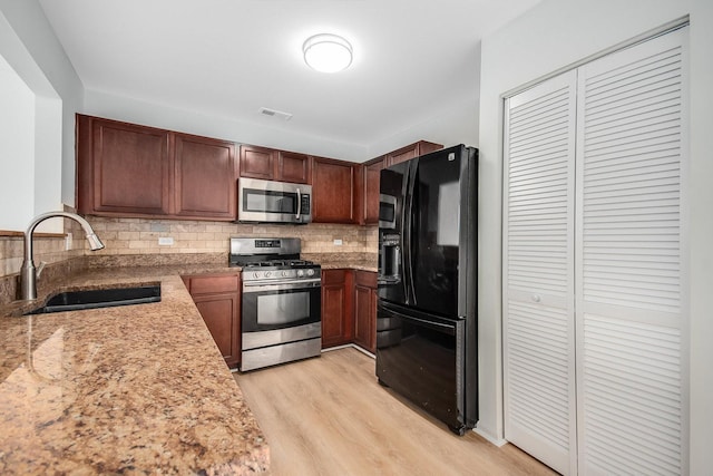 kitchen featuring appliances with stainless steel finishes, sink, backsplash, light stone counters, and light hardwood / wood-style floors