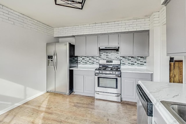 kitchen featuring gray cabinets, brick wall, tasteful backsplash, light hardwood / wood-style floors, and stainless steel appliances