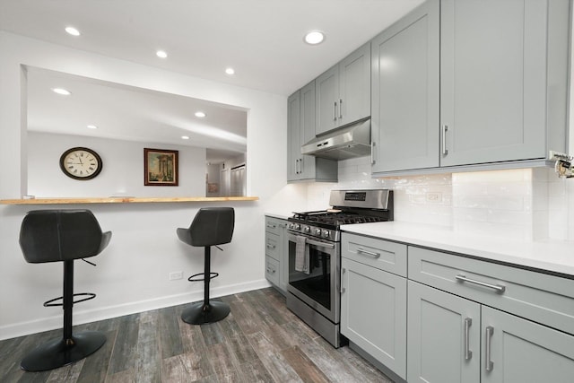 kitchen featuring gray cabinetry, a kitchen breakfast bar, dark hardwood / wood-style floors, stainless steel range with gas stovetop, and tasteful backsplash