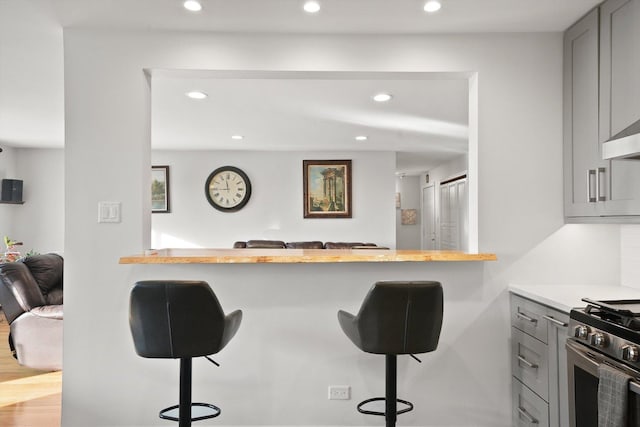 kitchen with gray cabinetry, a breakfast bar area, light hardwood / wood-style floors, kitchen peninsula, and stainless steel range with gas stovetop