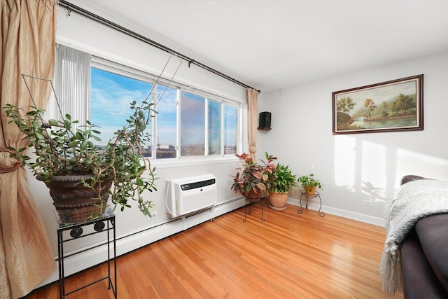 living area featuring a baseboard heating unit, hardwood / wood-style flooring, a wall mounted AC, and a healthy amount of sunlight