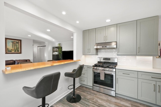 kitchen with tasteful backsplash, stainless steel range with gas stovetop, dark hardwood / wood-style flooring, and kitchen peninsula