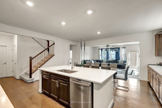 kitchen featuring dishwasher, sink, a kitchen island with sink, dark brown cabinets, and light wood-type flooring