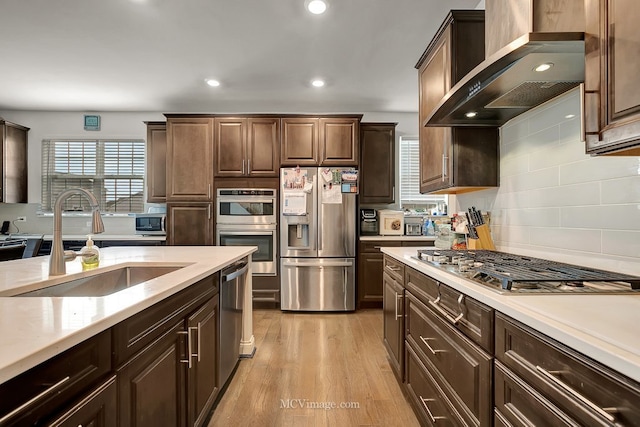 kitchen featuring wall chimney exhaust hood, dark brown cabinetry, sink, light hardwood / wood-style flooring, and stainless steel appliances