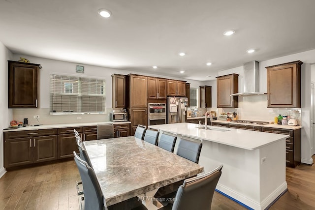 kitchen with stainless steel appliances, a kitchen island with sink, a breakfast bar, and wall chimney exhaust hood