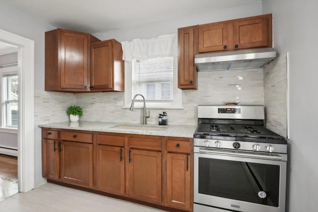 kitchen featuring sink, stainless steel gas range, baseboard heating, light stone countertops, and decorative backsplash